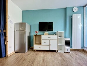 Ein Zimmer mit einer türkisfarbenen Wand, einem Flachbildfernseher, einem weißen Kleiderschrank, einer weißen Kommode und Holzboden.