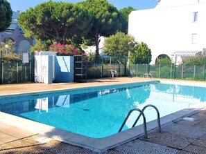 En swimmingpool med klart, blått vatten, omgiven av ett staket och träd.