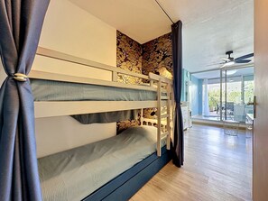 A bunk bed with a stone wall behind it, a ceiling fan, and a view of an outdoor patio. - Les Floralies II by Interhome (Le Grau du Roi)