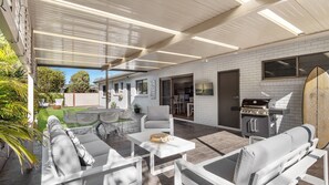 An outdoor patio with a grill, seating, and a surfboard. - Southcoast Haven is the perfect spot for your next getaway (Shoalhaven Heads)