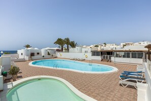 Ein Pool auf dem Dach mit Blick auf das Meer, umgeben von weißen Gebäuden und Palmen.