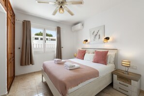 Ein Schlafzimmer mit Bett, Nachttischen, Deckenventilator und einem Fenster mit Vorhängen.