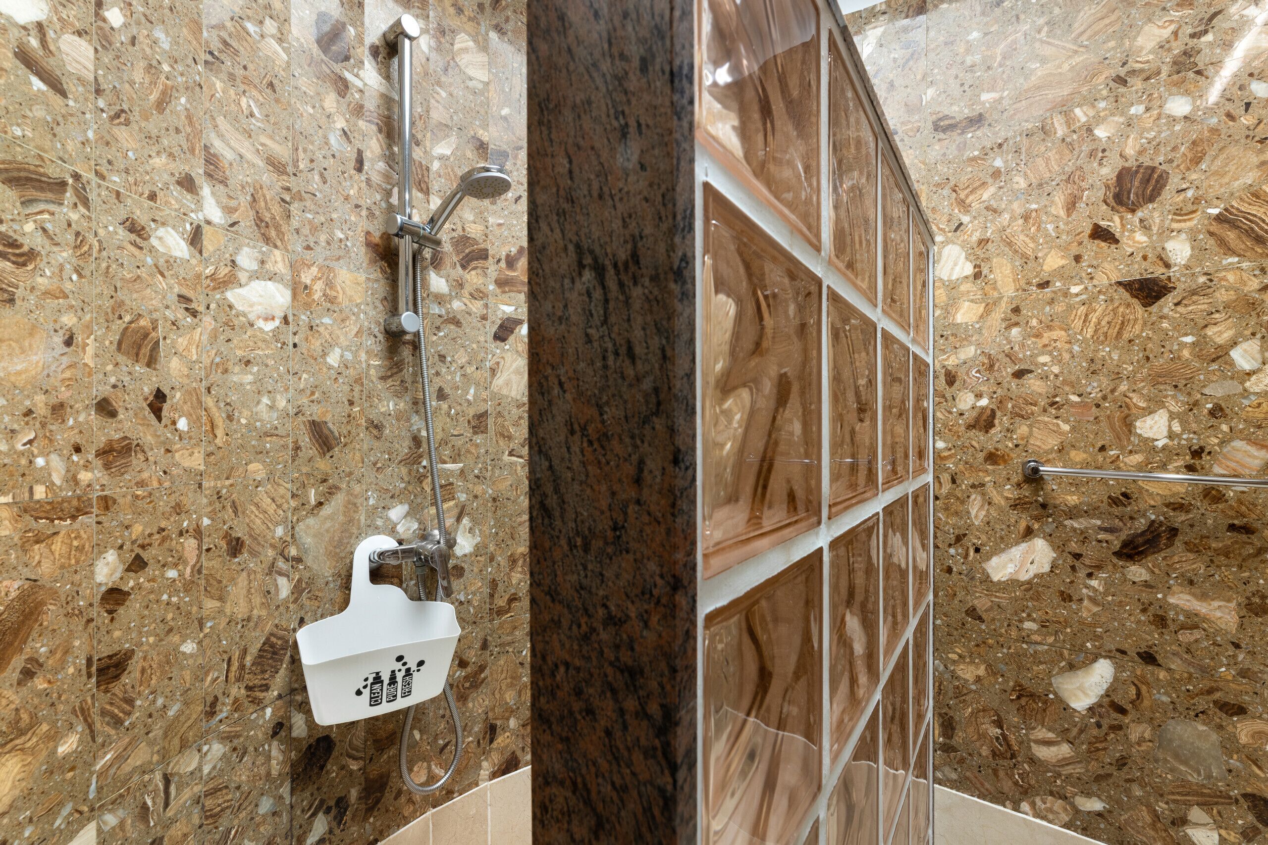 Un baño con piso de mármol, zona de ducha y pared con azulejos.