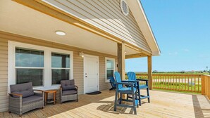 Une terrasse couverte, meublée avec des meubles en osier, dotée d’une porte et offrant une vue sur la plage.
