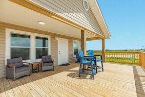 Eine überdachte Terrasse mit Korbmöbeln, einer Tür und Blick auf den Strand.