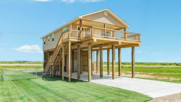 Une maison à deux étages dotée d’un balcon, d’une terrasse en bois et d’un escalier menant à l’étage supérieur.