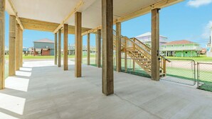 Un pavillon ouvert avec un sol en béton et des poutres en bois, un escalier et une vue sur des maisons en arrière-plan.