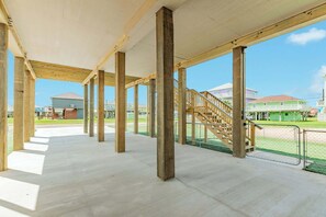 Eine offene Pavillonkonstruktion mit Betonböden und Holzbalken, eine Treppe und Blick auf Häuser im Hintergrund.