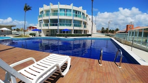 A swimming pool with lounge chairs, a modern building with balconies, and palm trees.