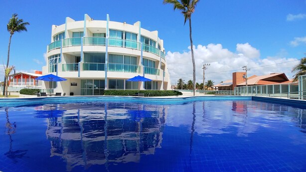 A modern hotel with a large pool, palm trees, and clear blue skies. - Ap com Wi-Fi, Ar, Máquina de Lavar e Piscina (Barra de São Miguel)