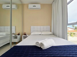 Quarto de hotel com cama, mesa de cabeceira, espelho, aparelho de ar condicionado e vista para palmeiras.