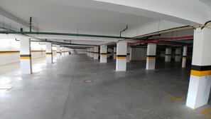 A multi-level parking garage with white pillars, yellow and black stripes, and visible pipes on the ceiling. - Apartamento 2 quartos VistaMar (Barra de São Miguel)