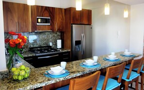 Eine moderne Küche mit Granit Arbeitsplatten, Holzschränken, Edelstahlgeräten und blauen Sitzgelegenheiten.