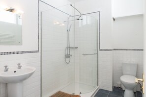 Et moderne badeværelse med et glasafskærmet brusebad, en hvid vask og et toilet.