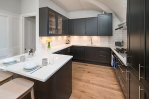 Uma cozinha moderna com armários escuros, bancada branca e piso de madeira.