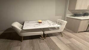 Uma área de refeições com mesa de mármore, duas cadeiras estofadas e uma pequena vela.