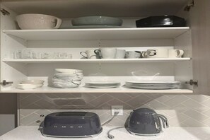 Eine Küche mit weißen Regalen, auf denen verschiedene Geschirrteile und ein Toaster stehen.