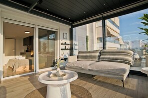 A modern living area with a sofa, a round table, and a view of a cityscape through large windows. - Riviera Sky Loft (Glifada)