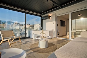 Ein modernes Interieur mit einer großen Glasscheibe, einem runden weißen Tisch mit Pflanze, einem Holzstuhl und einer Couch.