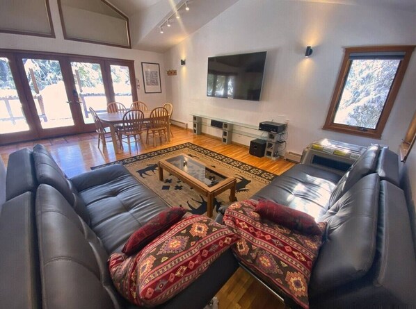 A living room with leather sofas, a glass coffee table, a flat-screen TV, and a large window.