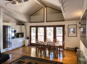 Una cocina moderna con refrigerador integrado, un comedor con mesa y sillas de madera, y ventanas amplias que dejan entrar luz natural.