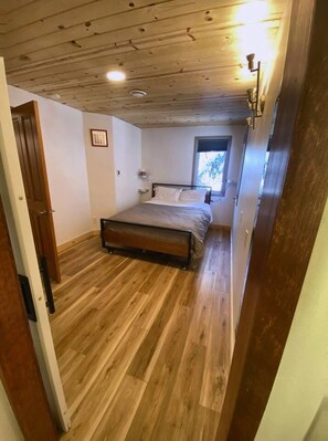A bedroom with a wooden floor, a bed, a window, and a door.