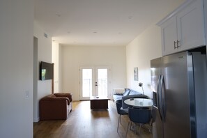 Eine moderne Küche mit einem Edelstahl-Kühlschrank, eine Essecke mit rundem Tisch und Stühlen, ein braunes Sofa und ein großes Fenster mit Blick.