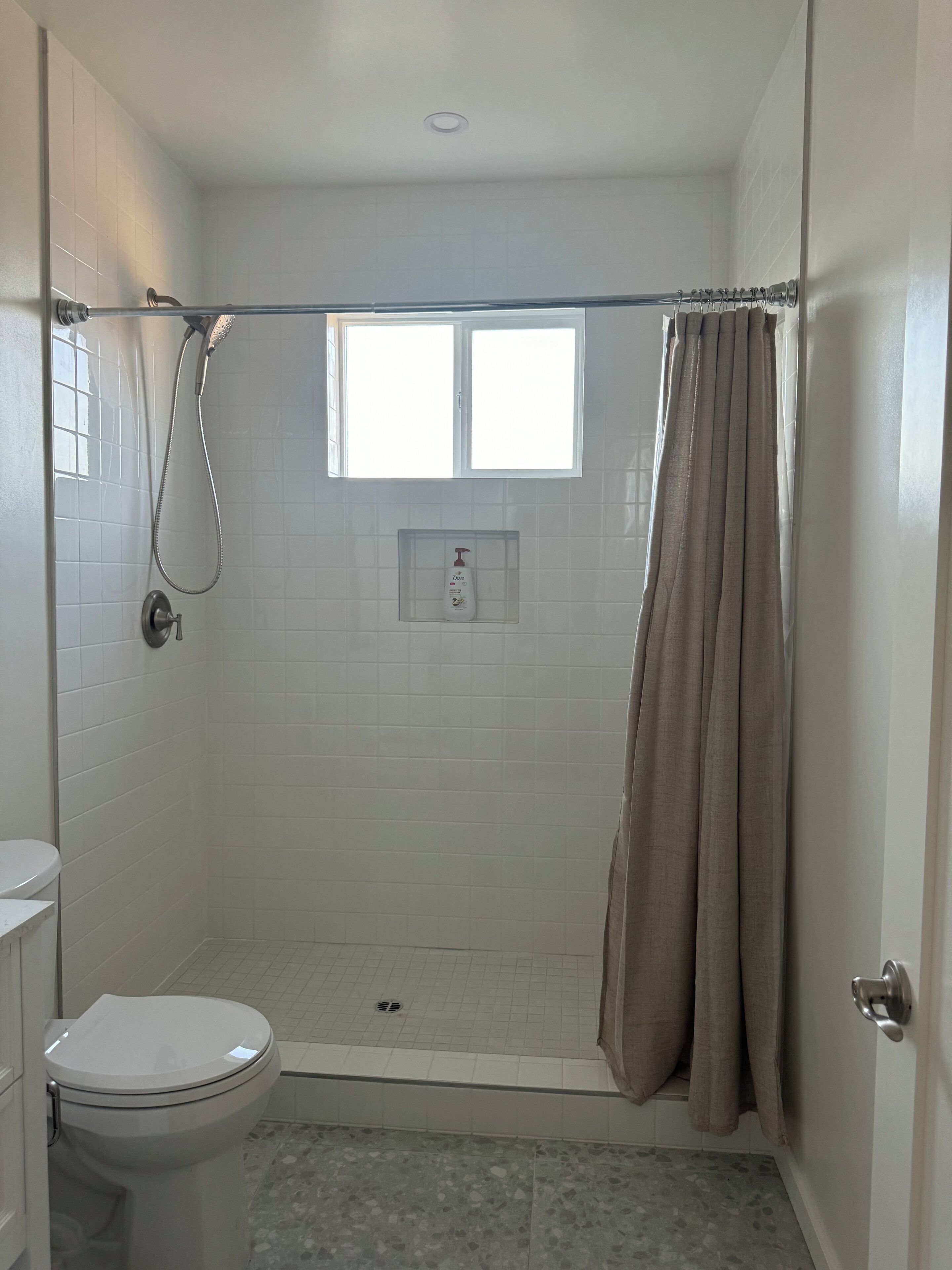 Ein Badezimmer mit Dusche, Toilette und Fenster.