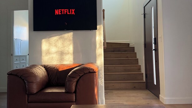 Ein Wohnzimmer mit braunem Ledersofa, einem flachbildfernseher an der Wand und einer Treppe, die zu einer anderen Ebene führt.