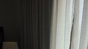 Ein Bett mit weißen Leinentüchern und einer schwarzen Schleife, eine Lampe sowie transparente Vorhänge.