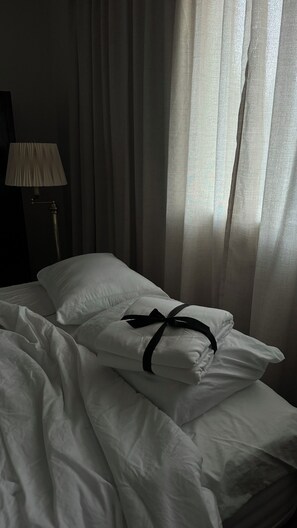 Ein Bett mit weißen Leinentüchern und einer schwarzen Schleife, eine Lampe sowie transparente Vorhänge.