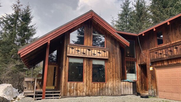 A wooden cabin with a sloped roof, large windows, and a garage. - Iconic A-Frame | Steps to Alyeska + Restaurants (Anchorage)