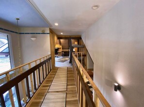 A staircase with wooden railings leading to a bedroom with a bed and a nightstand.