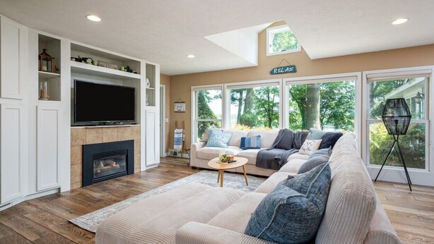 Una sala de estar con un sofá modular, un televisor de pantalla plana, una chimenea y un ventanal con vistas a árboles.