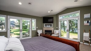 Un dormitorio con una cama grande, puertas correderas de vidrio a un jardín trasero, chimenea y televisor montado en la pared.