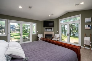 Ein Schlafzimmer mit einem großen Bett, Schiebeg lass Türen zum Garten, einem Kamin und einem an der Wand befestigten Fernseher.
