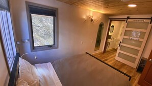 A bedroom with a bed, a window, a door, and a mirror.