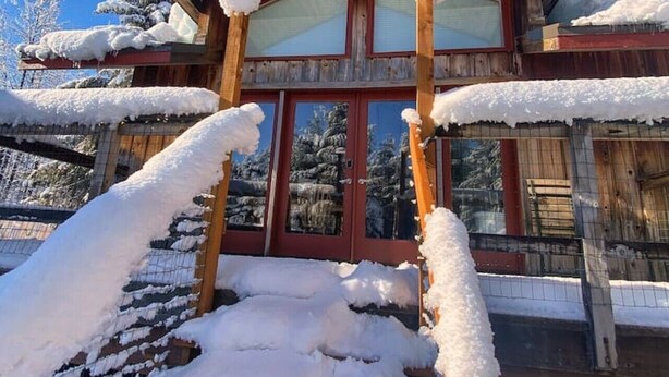 A wooden building with a red door and windows, surrounded by snow-covered steps and trees.