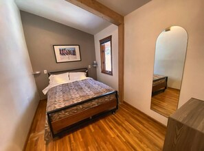 A bedroom with a bed, a window, a mirror, and a wooden floor.