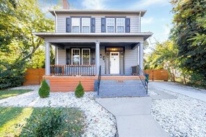 A two-story house with a front porch, a small front yard, and a wooden fence.