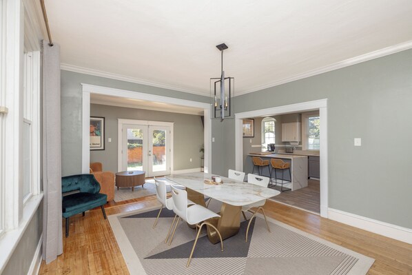 A spacious dining area with a marble table, white chairs, and a teal sofa.