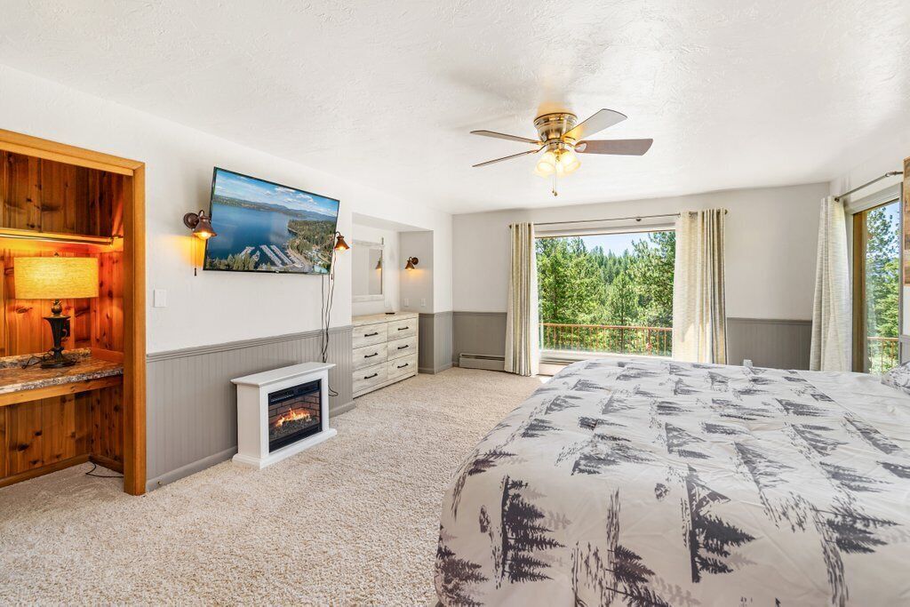 Une chambre avec une cheminée, un ventilateur de plafond, un grand lit, une télévision et une vue sur les arbres par la fenêtre.