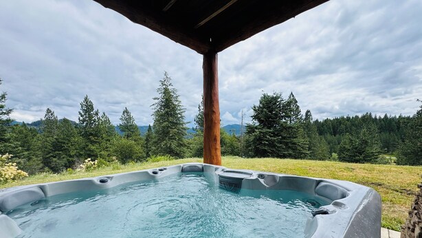 Un bain à remous doté d’une structure en bois au-dessus, entouré d’un paysage naturel avec des arbres et des montagnes.