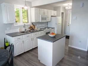 A modern kitchen with white cabinetry, a central island, and a microwave above the stove.