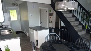 Una cucina moderna con lavastoviglie integrata, una zona pranzo con un tavolo rotondo e sedie, e una scala con ringhiera in metallo.