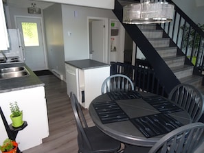 Eine moderne Küche mit Geschirrspüler, einem Essbereich mit rundem Tisch und Stühlen sowie einer Treppe mit Metallgeländer.