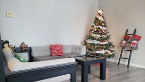 Un soggiorno con un divano grigio, un tavolino, un albero di Natale e una scala con calze appese.