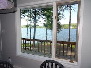 A room with a large window overlooking a lake, a wooden deck, and a chair.