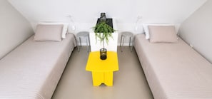 Une chambre avec deux lits, une petite table jaune, une plante en pot et une étagère fixée au mur.
