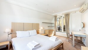 Ein Hotelzimmer mit Bett, Nachttischen, Schreibtisch, Stuhl und einem Vorhangfenster.